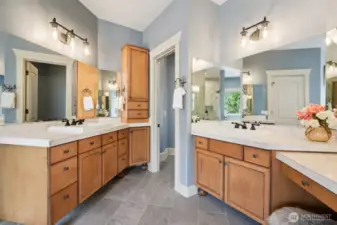 Tailored for comfort and elegance, this ensuite features dual vanities with richly toned maple cabinetry, sleek stone counters, and expansive mirrors that reflect soft natural light. A full-height linen tower offers smart storage, while a discreetly tucked-away water closet enhances privacy. The thoughtful layout balances form and function, delivering spa-level luxury for your daily rituals