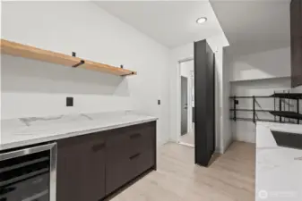 Murphy door leading to walk-in pantry with wine cooler, prepping counter space, cabinets, sink and storage shelving.