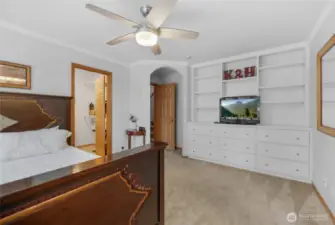 MAIN FLOOR primary bedroom is large with built-in dresser and shelving area. There are also large windows looking into the backyard. The bedroom has a ceiling fan, a walk-in closet, and an attached five-piece bathroom