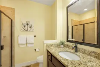 Main level three-quarter bath with upgraded granite slab countertops, tile floor and tile shower surround.
