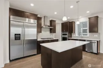 Gourmet kitchen with large center island, eating area, loads of cabinets with soft close, built-in 48" fridge and gas cooktop. Photo is representational. Actual home is under construction and materials, colors, and finishes will vary. See site agent for details.
