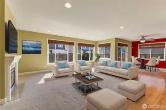 The great room offers a comfortable and inviting space with a cozy gas fireplace framed by a classic white mantle and tile surround. Large windows provide plenty of natural light and a lovely view of the fenced, landscaped backyard.