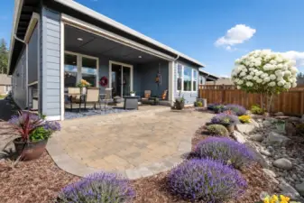 Lavender is just about to bust out (this is AI but the shrubs really are there). Wonderful rock drainage, pavers, covered patio with electronic screens...WOW - JUST WOW!