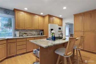 Large kitchen with slab granite countertops, full backsplash, center island and a desk area.