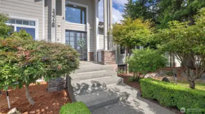 Grand entryway framed by lush greenery, featuring elegant double glass doors and a striking transom window above!