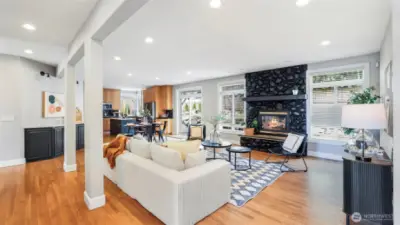 This vast open-concept space combines the living room, kitchen, dining area, and a charming nook—highlighted by warm wood flooring and a bold, stone-accented feature fireplace that adds character and charm
