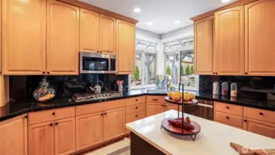 The kitchen showcases sleek black granite tile countertops, warm wood cabinetry, a spacious open layout, a double sink, a large window above the sink that brings in natural light, and a stylish backsplash