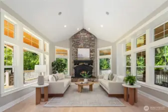 Grand living room wrapped in windows, featuring a striking floor-to-ceiling stone fireplace.