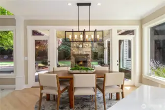 A bright, modern dining space framed by large windows that open to the patio & lush greenery.