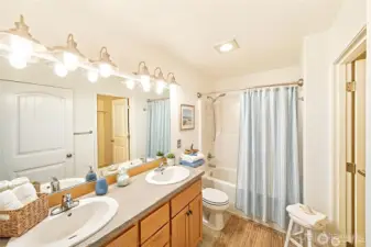 The primary bathroom features a spacious double-sink vanity, bright lighting, and a full tub-shower combination with a fresh, coastal feel.