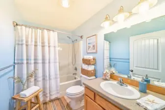 This bathroom features a fresh, coastal feel with soft blue walls, a full tub-shower combination, and a spacious vanity with bright lighting.