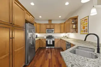 Custom cabinetry, in a warm hue perfectly complimented by slab granite counters and stainless appliances, offers storage and plenty of counter space. To the left of the refrigerator, a pantry awaits. The refrigerator and gas range are brand new.