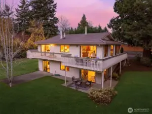 Twilight gathers around this secluded Newcastle retreat as warm interior light reaches out across the pastoral lawn and into the trees at the woodland edge. The home’s elevated deck and garden-level patio create inviting spaces to take in the quiet, the privacy and the changing skies.