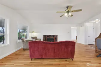 Living room with freestanding electric fireplace, large windows and oak hardwood floors.