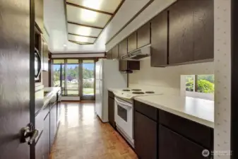 Period galley kitchen featuring original solid oak wood parquet flooring. The pass-through is visible, with the eating area in the background.