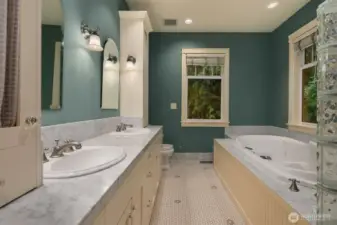 Five-piece primary bathroom has double vanity with Carrera marble counters and floor trim, heated tile floor, luxury shower system and drop-in jetted tub with tile surround