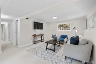 A wide, multi-paned window draws in natural light, softening the lower level and giving the room an open, comfortable feel throughout the day. Overhead, a softly glowing ceiling light keeps the space bright and welcoming in the evenings, adding an easy warmth after sunset.  Bright modern sconces adorn the wide hallway, with matching brushed nickle finishes throughout.   This versatile space easily becomes a cozy sleepover retreat, a lively game room, or a relaxed play space. There’s room to spread out, gather, and unwind, with enough openness to adapt as needs change over time.