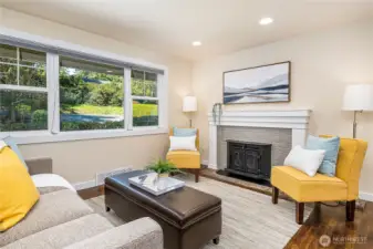 The front living room welcomes you as you enter, filled with natural light from two skylights and large windows that offer serene views of the front yard. A fireplace with insert adds warmth and comfort for cozy winter days.