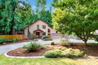 Framed by tall trees and fresh landscaping, the home’s front profile showcases Northwest charm with its wood siding, dual garage, and inviting covered entry.