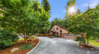 A tree-lined gravel driveway winds its way toward this private Geneva retreat, where curated landscaping and towering evergreens create a serene woodland welcome.