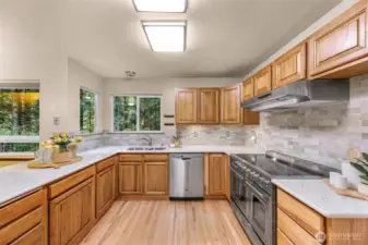 This polished chef’s kitchen showcases a luxury gas range, sleek quartz countertops, and full-height tile backsplash. Oversized windows fill the space with light and nature.