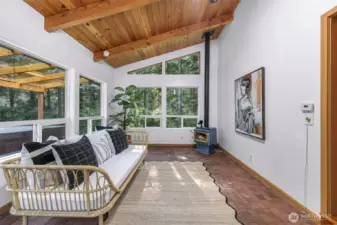 A second angle of the sunroom reveals its connection to the outdoor deck and the home’s natural setting. Floor-to-ceiling windows bring the outside in, while the wood-paneled ceiling adds warmth overhead.
