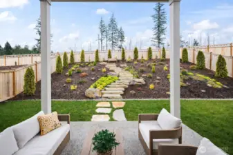 Professionally landscaped backyard on a premium lot in McCormick Trails featuring outdoor living space, curated seasonal color, and seamless indoor-outdoor flow from the wall of windows — a rare finished yard for newer construction in Port Orchard.
