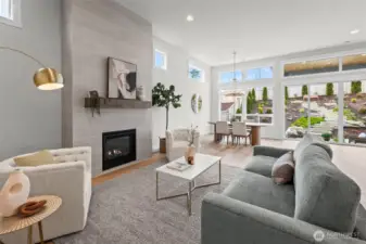 Open-concept living room featuring a dramatic floor-to-ceiling tiled fireplace and designer finishes, filled with natural light from oversized windows and seamlessly connected to the upgraded newer construction layout in McCormick Trails, Port Orchard.