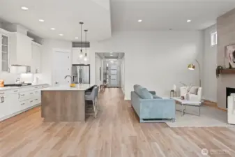View from the wall of windows looking toward the front entry, showcasing the open-concept layout where the upgraded kitchen and living room come together in a light-filled newer construction home in McCormick Trails, Port Orchard.
