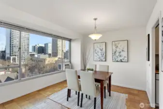 A true dining area set beside the windows—easy meals, open sightlines, a little peek toward the city, and a window A/C unit for warm days.