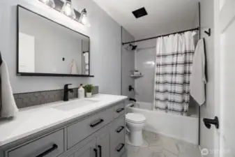 Upstairs features a full bathroom, with a modern vanity, tile floors and a tile surround shower.