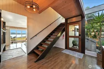 Step into an inviting entry where warm hardwood floors meet expansive floor-to-ceiling windows, offering stunning natural light and gentle glimpses of the shoreline beyond.