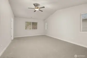 Spacious primary bedroom features vaulted ceilings, large windows for natural light, and a ceiling fan for added comfort.