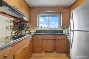 The kitchen features laminate flooring, wood cabinets, stainless steel appliances, and a large window with a view of the backyard and Bellevue skyline.