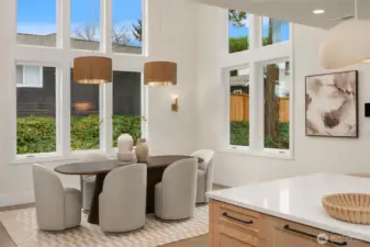 Light-filled dining area featuring soaring over 18 foot ceilings and open sightlines visible from the upper level.