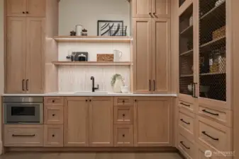 pacious walk-in pantry featuring custom cabinetry, open shelving, integrated sink, and built-in microwave for effortless organization.