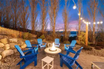 Twilight view of the home's outdoor entertaining area w/ built-in stone propane fire pit & seating area w/ stunning west-facing uplake views of Lake Chelan.
