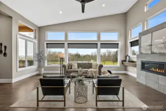 The living room features tall windows that frame open views while filling the space with natural light. A modern fireplace and open concept layout create a bright and welcoming living area designed for both entertaining and everyday comfort.