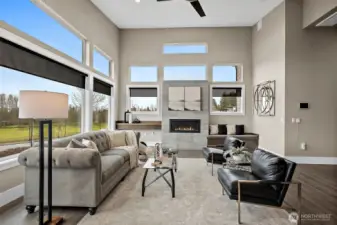 Bright, open living room in a modern home for sale in the River Rock community, featuring floor to ceiling windows, a contemporary fireplace, and abundant natural light. The spacious layout and scenic outdoor views create an inviting space ideal for relaxing or entertaining.
