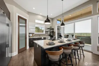 Modern kitchen in a home for sale in the River Rock community, featuring a large center island with seating, quartz countertops, stainless steel appliances, and sleek cabinetry. The open layout, abundant natural light, and connection to the living area create an ideal space for cooking, gathering, and everyday living.