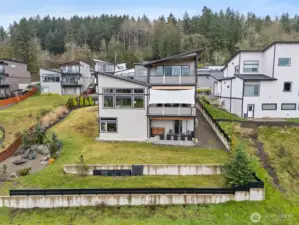 Modern exterior of a contemporary home for sale in the River Rock subdivision, featuring clean architectural lines, stone accents, a spacious driveway, and attached garage. Aerial and front views highlight its setting within the scenic River Rock community surrounded by natural greenery.