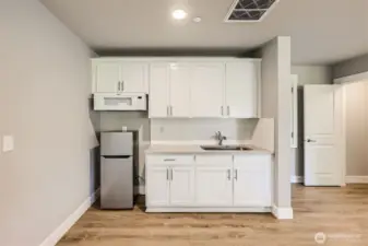 Kitchenette in lower living quarters. Stainless steel sink, microwave, refrigerator and DEEP walk-in storage space under the stairs would make a great pantry or closet.