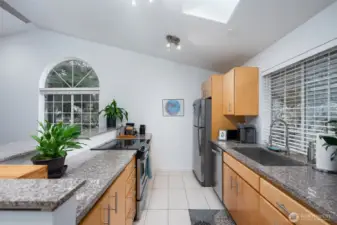 The kitchen is filled with natural light, featuring a window above the sink and a skylight overhead.