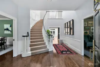 Foyer with hardwood floors throughout the main level.  One of two staircases with dining room on the left and living room/lounge on the right.