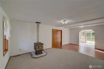 From the main entrance looking through the living room and dining room into the sun room and back deck. The double doors go to the main floor primary suite. The wood stove supplies supplemental heat.