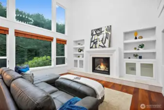 The great room features soaring 2-story ceilings and a custom gas fireplace surround with a tile hearth and art/media niches on either side.