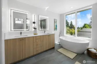 Luxe primary bath retreat: dual floating vanities, sculptural soaking tub, and treetop views. Photos are of model home 8825, finishes and floorplan may vary.