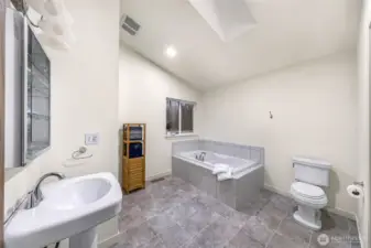 Spa-like en suite bath features soaking tub, vaulted ceiling, and peaceful views.