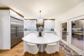 Kitchen reveals seamless flow between prep, dining, and outdoor access with island sink and custom hood.