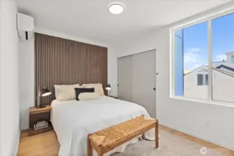 The serene primary suite offers a custom slatted wood feature wall, generous closet storage, and expansive natural light.